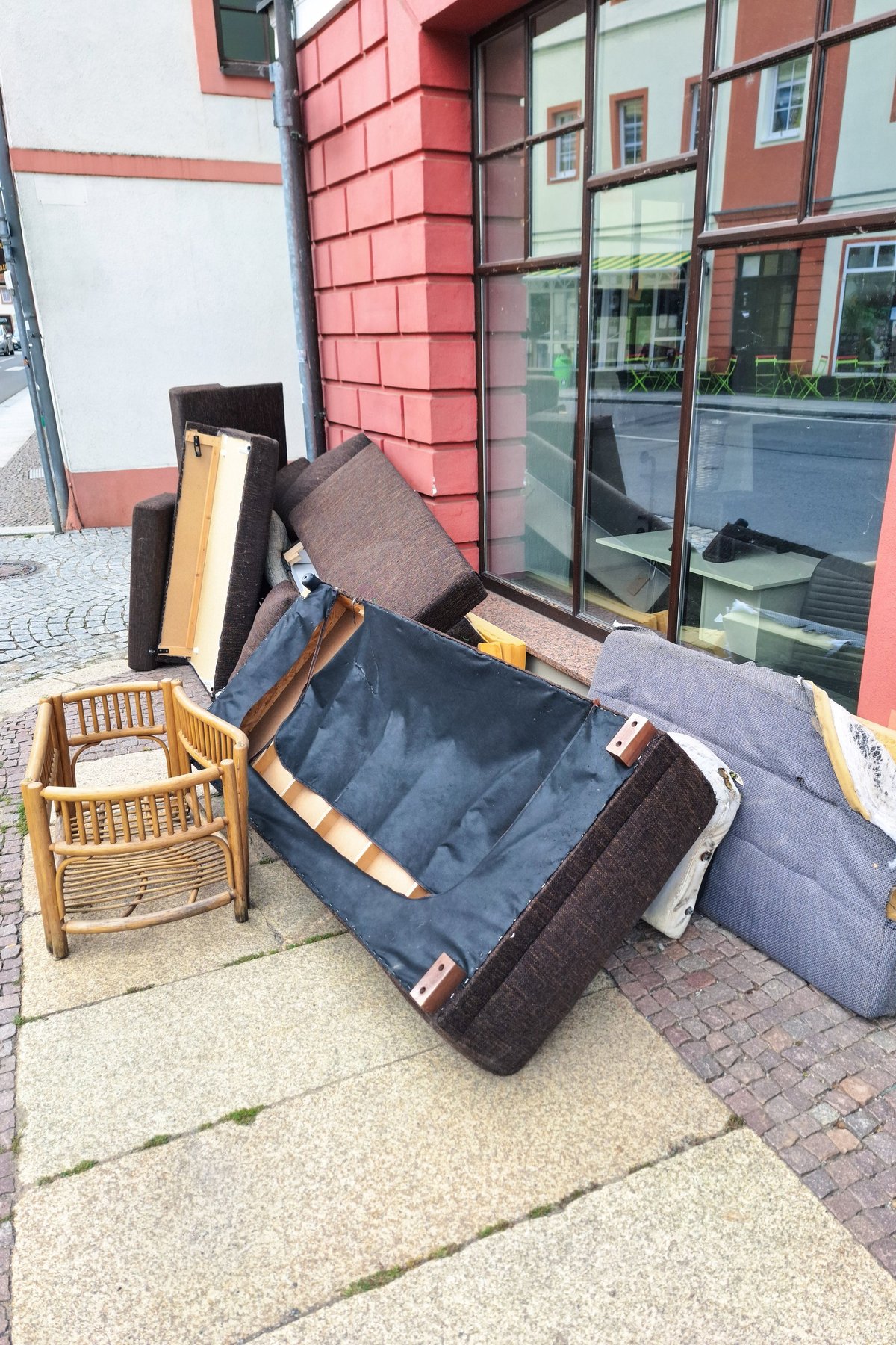 A pile of discarded furniture including a sofa, chair, and various cushions on a city sidewalk, highlighting urban waste and the need for proper disposal or recycling