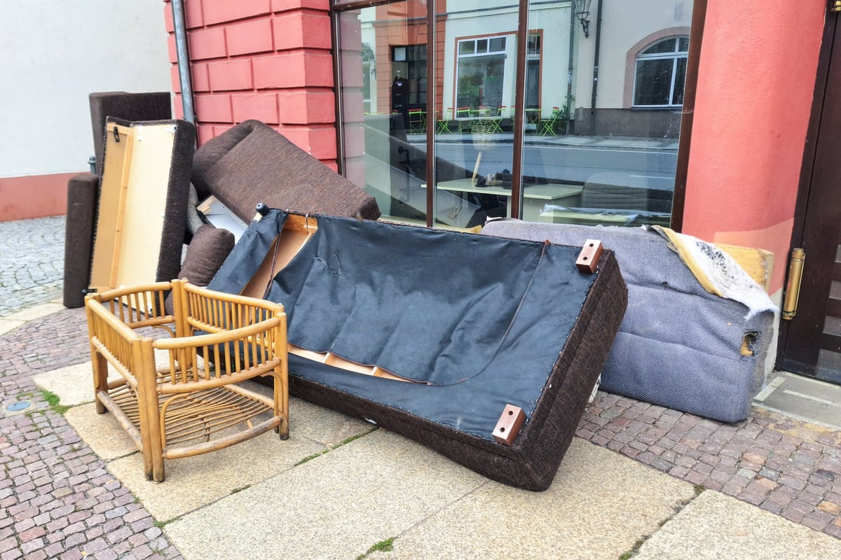 A pile of discarded furniture including a sofa, chair, and various cushions on a city sidewalk, highlighting urban waste and the need for proper disposal or recycling
