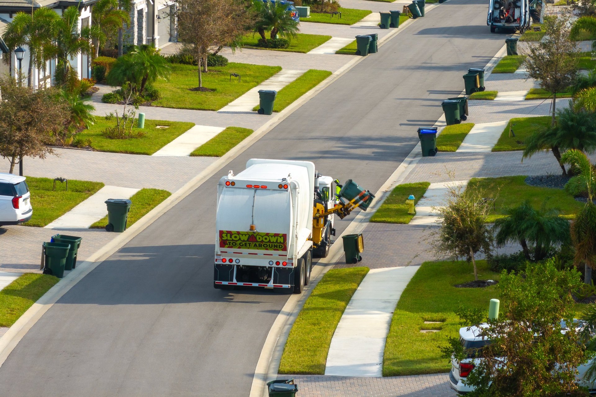 Garbage truck picking up trash bins on suburban street side