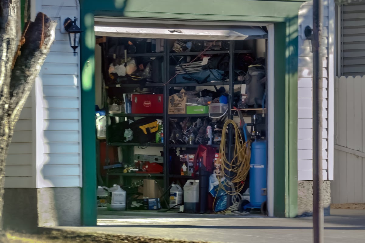 Cluttered residential garage filled with various tools, storage shelves, and household equipment in a suburban home