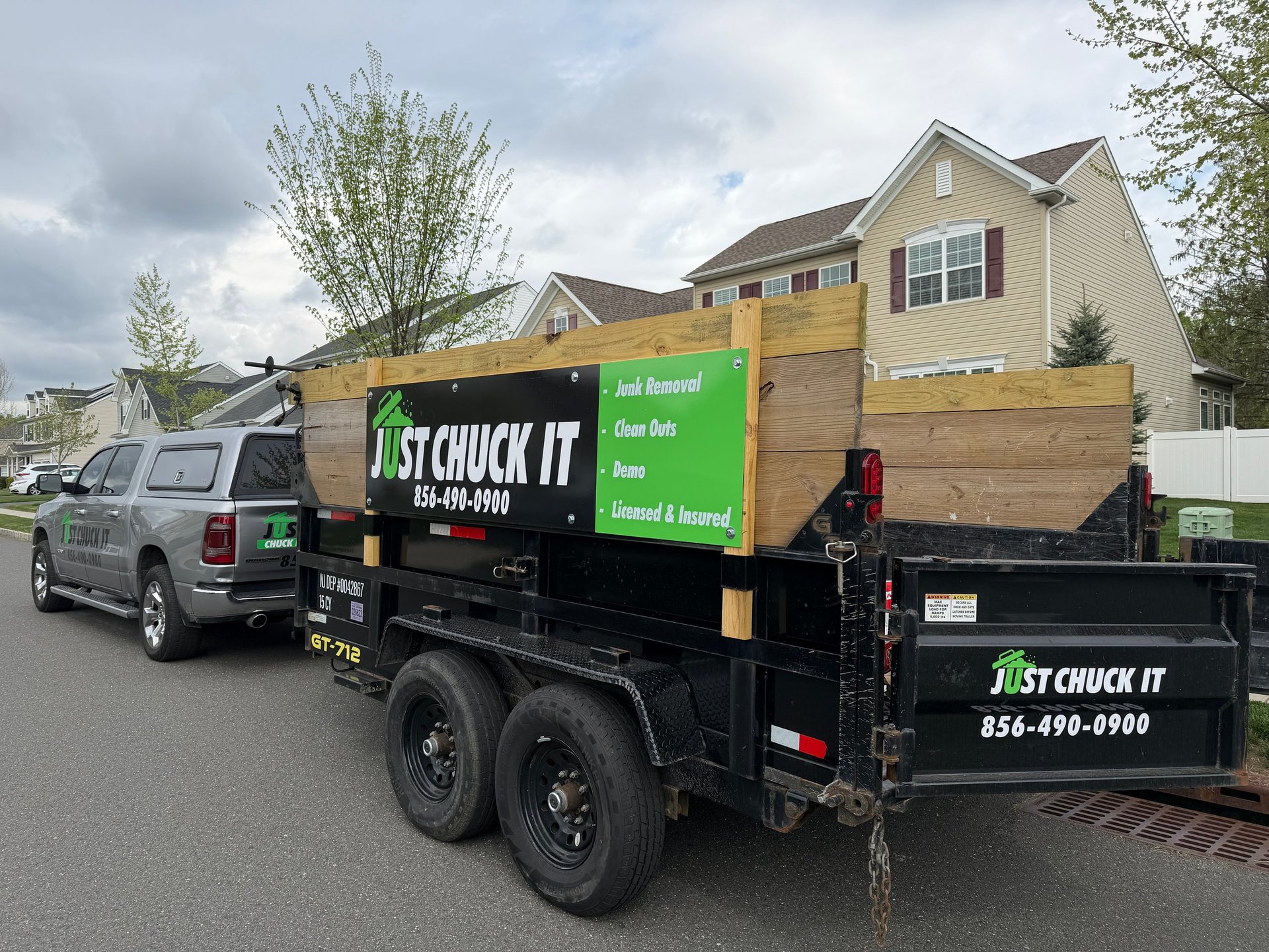 Junk removal truck parked in residential driveway with yellow and black branding and company phone number visible